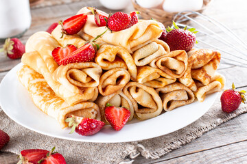 Plate with delicious thin pancakes with strawberries on table
