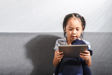 A young small kid Asian girl using her mobile tablet to play games, online learning, chatting or...