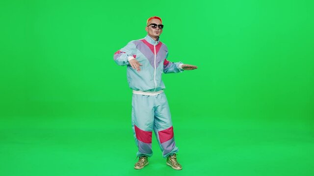 Pretentious retro guy in a multicolor suit dancing to the music on a green background, young digital influencer creates content, chromakey template.