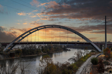 Fototapeta na wymiar a majestic aerial shot of the John Seigenthaler Pedestrian Bridge over the Cumberland River with powerful clouds at sunset with autumn trees in Nashville Tennessee USA