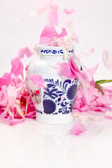 Decorative jar with blue floral patterns sprinkled with pink peony petals