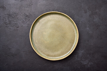 Empty green rustic ceramic plate with black rim on a light textured graphite background, flat lay,...