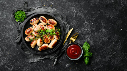Mini grilled sausages on a frying pan. Barbecue. Meat menu. Top view. On a stone background.