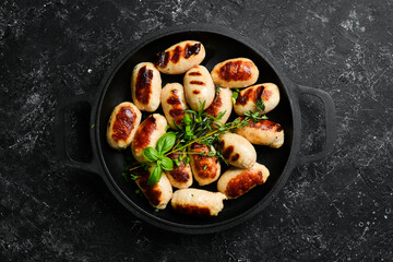 Mini grilled sausages on a frying pan. Barbecue. Meat menu. Top view. On a stone background.