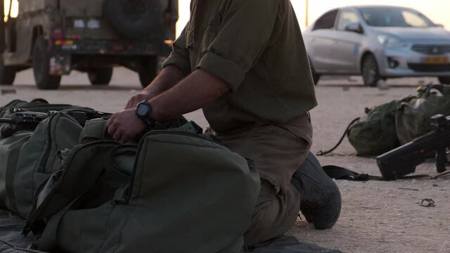 Close-up of soldiers hands prepare his equipment in his military bag ready to war while in the backround there are some vehicles