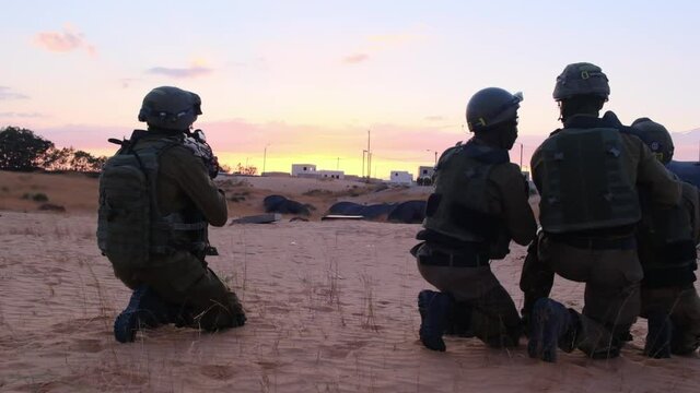 Slow motion of a team of combat soldiers planning its raid on a sandy desert area at sunset