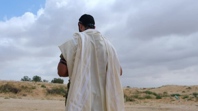 A religious Jew soldier prays with a tallit and tefillin on him in the morning at a military camp in a desert and sickness area