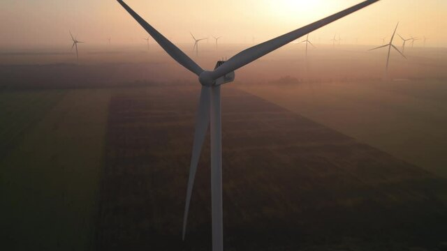 Close-up of wind turbine blades at sunset or sunrise. Windmills with rotating wings among green fields. Technology for wind energy, renewable energy source, earth care. Wind power station, drone video