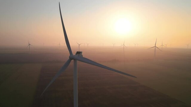 Close-up of wind turbine blades at sunset or sunrise. Windmills with rotating wings among green fields. Technology for wind energy, renewable energy source, earth care. Wind power station, drone video