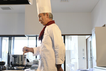 飲食店の厨房でコック服を着たシニア男性が料理を作る