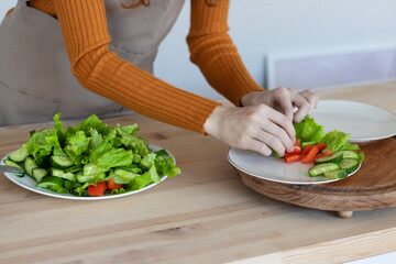 young girl in an apron makes a healthy salad of vegetables and herbs in her kitchen