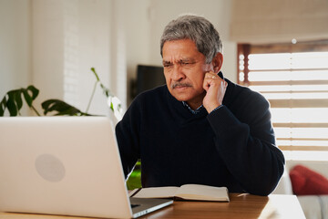 Concerned Multi-cultural elderly using laptop. Isolating in modern home, sitting at kitchen counter top.