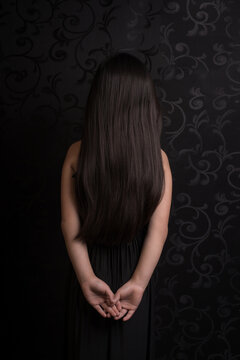 Fine art studio portrait of rear view of girl in dress with long black hair in the dark