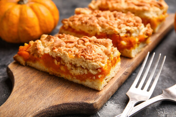Wooden board with pieces of tasty pumpkin pie on black background, closeup