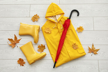 Umbrella, rubber boots, raincoat and autumn leaves on light wooden background