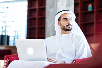 Handsome man with dish dasha working in his business office of Dubai. Portraits of a successful businessman in traditional emirates white dress. Concept about middle eastern cultures