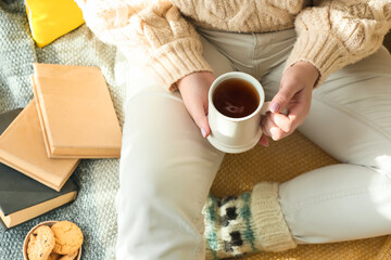 Young woman with cup of tea sitting on plaid in room