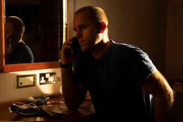 A middle-aged man calls on a mobile phone while waiting for the results of a covid-19 pcr test, self isolate, in a hotel room near Manchester airport, UK