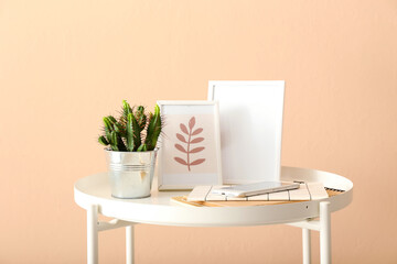 Potted cactus, notebooks, mobile phone and picture frames on table against color wall