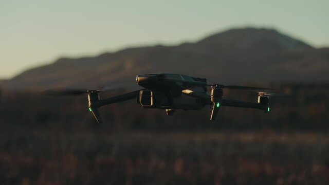 Modern Quadcopter Hovering Over Fields With Bokeh Mountains Background. Selective Focus