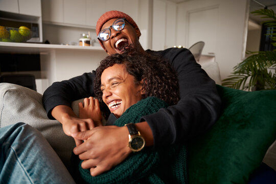 Trendy multi-ethnic adult couple sitting on sofa laughing hysterically. High quality photo