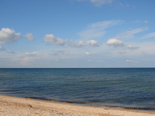 Obraz premium Panorama of the sandy beach near the crystal clear waters of the calm sea on a background of barely cloudy evening sky.