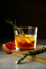 Whiskey sour cocktail with rum ice grapefruit and rosemary in shot glass on book. Alcohol cocktail in light beam