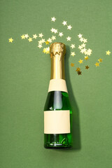 Bottle of champagne and confetti on green background