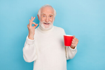 Photo of funky aged grey hairdo man show okey hold espresso wear white jumper isolated on blue color background