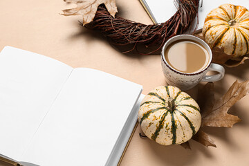Cup of tasty coffee, blank book, pumpkins and autumn leaves on beige background