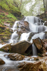 Waterfall in a spring forest with river stone boulders on a rocky hilly area.