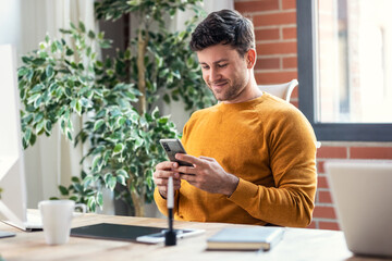 Graphic designer working with computer while using smartphone in modern startup office.