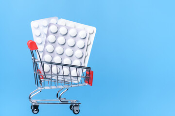 Shopping trolley cart with pills in a blister pack on blue background. Drug delivery. Medicine and...