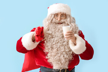 Santa Claus with glass of milk and red bag on blue background