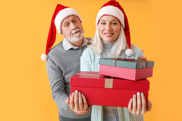 Happy mature couple in Santa hats and with Christmas gifts on color background