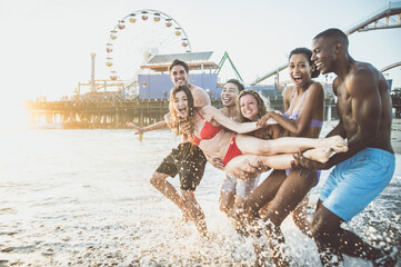 Storytelling image of a group of friends spending time in Santa Monica playing and having fun. Multiethnic young people from california reunited on the beach during a summer day. - obrazy, fototapety, plakaty