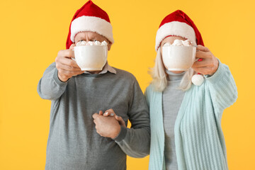 Fototapeta na wymiar Happy mature couple in Santa hats and with hot chocolate on color background