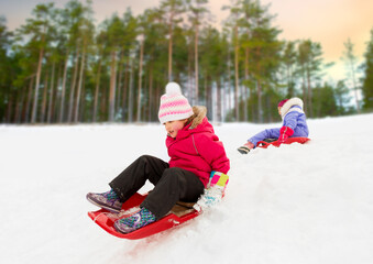 Fototapeta na wymiar childhood, sledging and season concept - happy little girl sliding down on sled outdoors in winter over snowy park or forest background