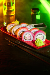 Assorted sushi rolls on plate and drink served on bar counter lighted by LED strip