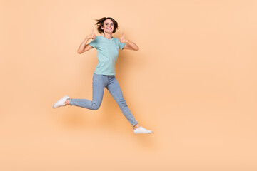 Fototapeta na wymiar Full body photo of young excited girl jump show thumb-up perfect suggest ads isolated over beige color background