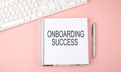Pink office desk with keyboard and notebook with text ONBOARDING SUCCESS