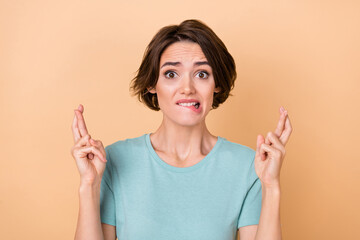 Photo of young woman anxious bite lisps crossed fingers pleading isolated over beige color...