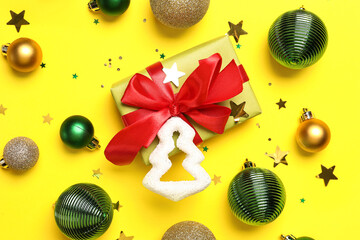 Composition with Christmas gift and balls on yellow background