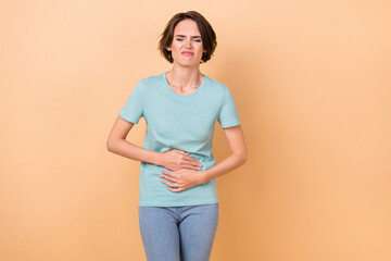 Photo of young woman feel bad spasm hands on stomach disease ill isolated over beige color...