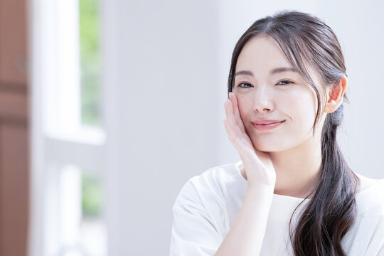 お肌の調子を気にして微笑む美しい若いアジア人(日本人）女性 クローズアップ　コピースペースあり