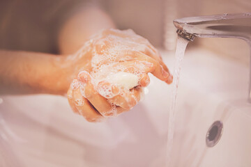 A man washes his hands with soap over a white ceramic sink next to an open faucet and a stream of water. Hygiene in the bathroom. Clean hands.