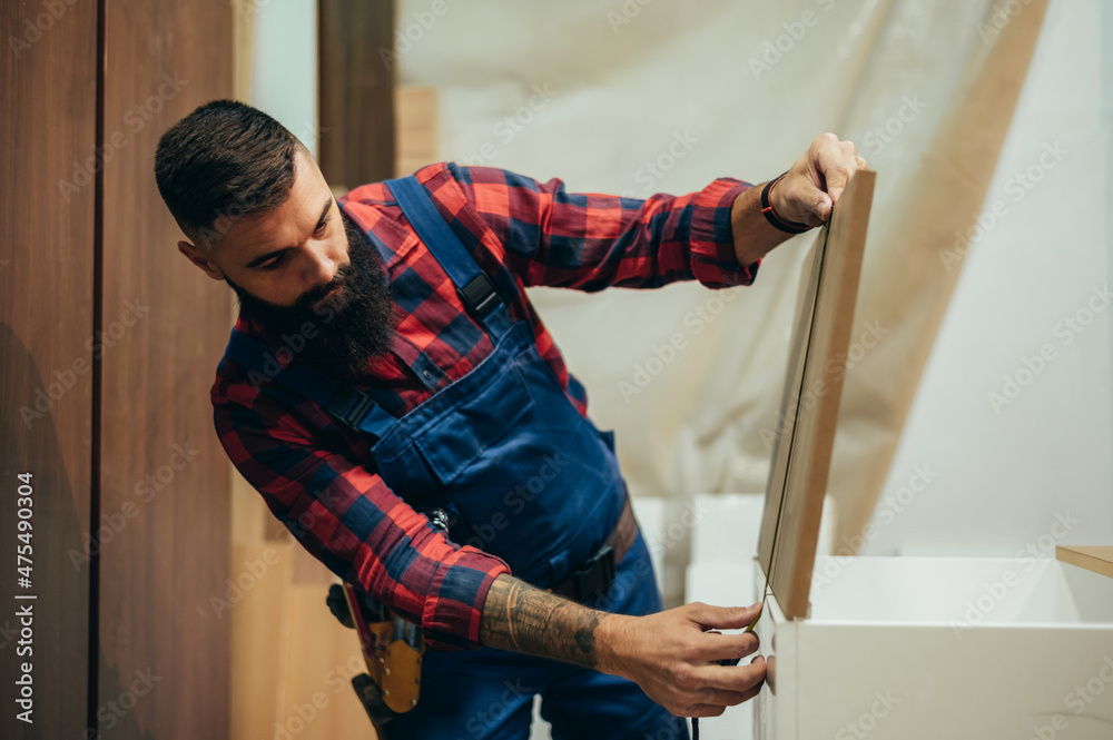 Wall mural Young male carpenter working in workshop and measuring with meter