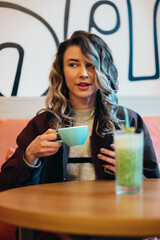 Beautiful young woman drinking coffee and using smartphone in a cafe