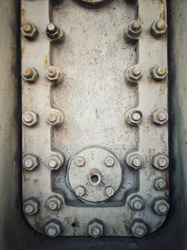 Rusty steel hatch door secured with nuts and bolts