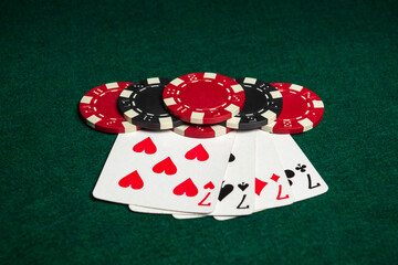 Poker game with four of a kind or quads combination. Chips and cards on green table. Successful and win four sevens